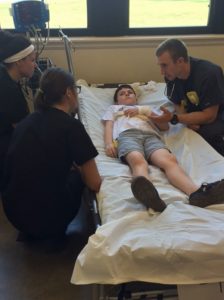 Three health professions students surround a child on a hospital bed practicing assessments procedures.