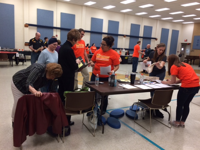 This image shows students in health professions t-shirts engaging with patients during a health fair at a local senior center.